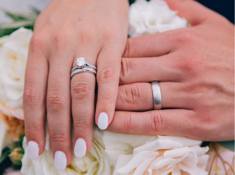 Sposo con fede nuziale in oro bianco mano nella mano con la sposa con anello di fidanzamento solitario